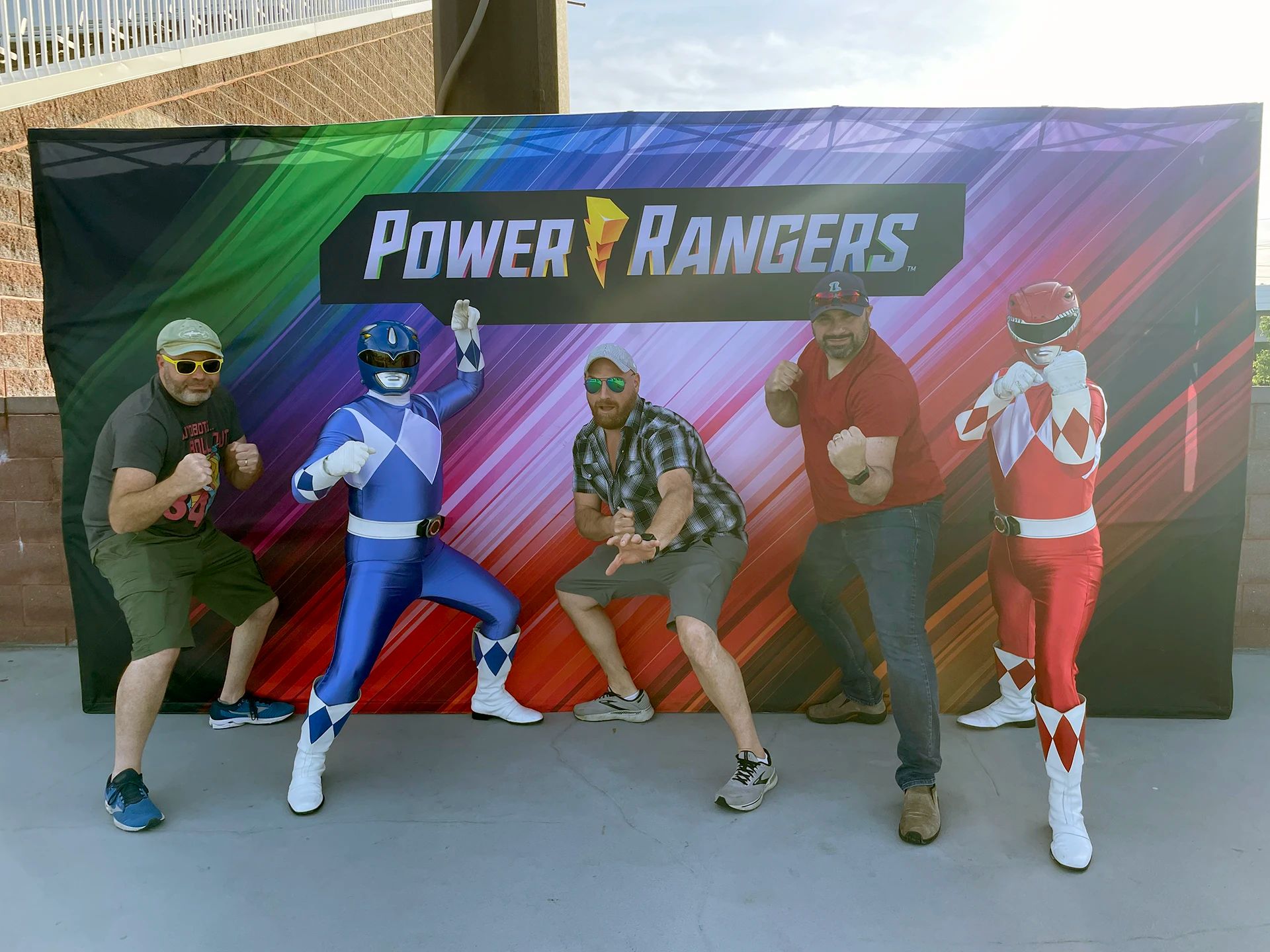 Fans posing with Power Rangers outside in front of a backdrop